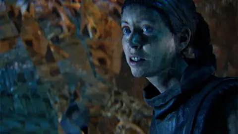 忍者理论 一个由电脑生成的、照片般逼真的女性角色在镜头外窥探到某物时露出了恐惧的表情。她似乎处于某种潮湿的洞穴环境中。
